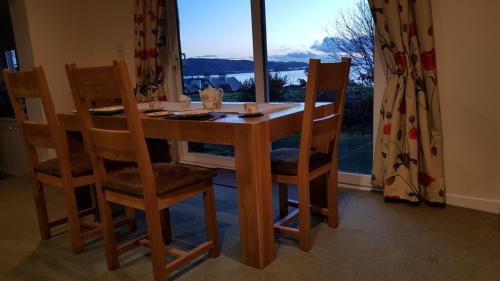 a dining room table with four chairs and a window at The Old Cottage in Arduaine