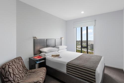 a bedroom with a bed and a chair and a window at Nesuto St Martins Apartment Hotel in Auckland