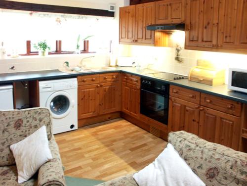 cocina con armarios de madera, lavadora y secadora en Brook Cottage, en Gillingham