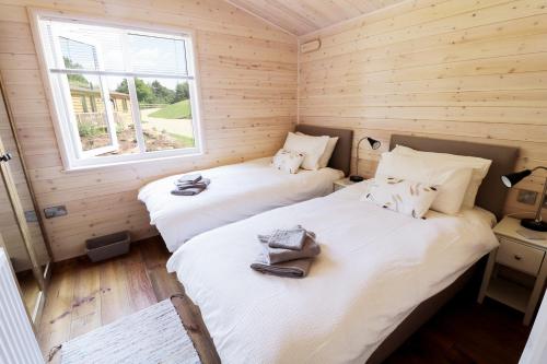 two beds in a room with wooden walls and a window at Skylark in Upton Bishop