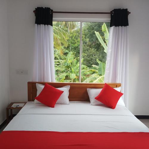 a bed with red and white pillows in front of a window at Cassia Udawalawe in Udawalawe