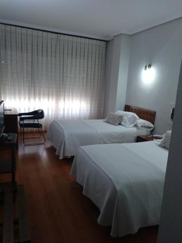 a hotel room with two beds and a desk at Hotel Marqués de Santillana in Torrelavega