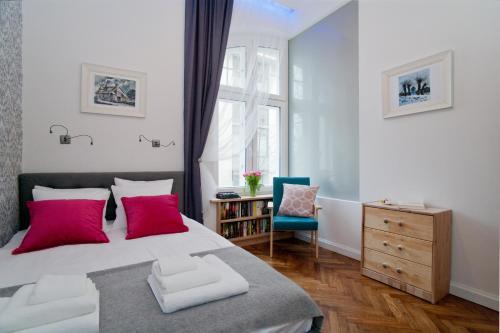 ein Schlafzimmer mit einem Bett mit rosa Kissen und einem Stuhl in der Unterkunft Kurkowa Apartments in Krakau