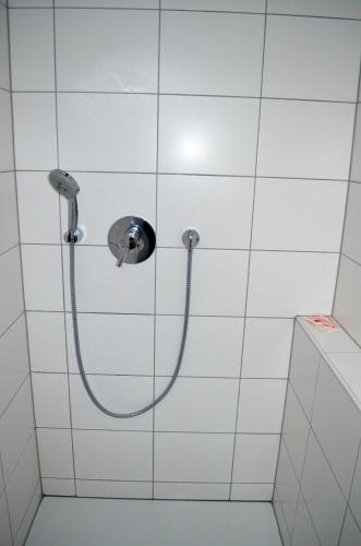 a shower with a hose in a white tiled bathroom at Beim Hooch "Schindelloft" in Brücktal