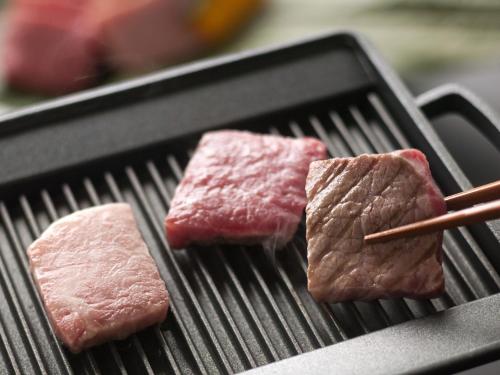 two pieces of meat cooking on a grill with chopsticks at Honjin Hiranoya Kachoan in Takayama