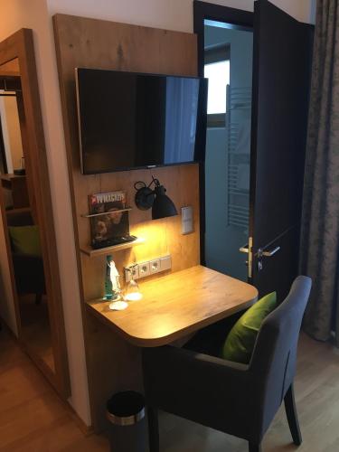 a desk with a chair and a television on a wall at Parkhotel Leiser in Planegg