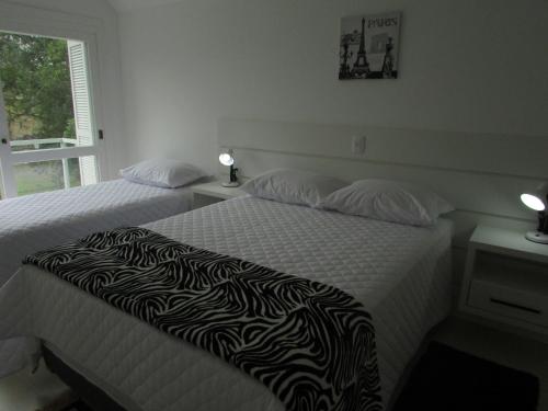 a bedroom with two beds with white sheets and a zebra blanket at San Clemente Residence in Gramado