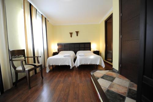 a hotel room with two beds and a chair at Hotel Montearoma in Valverde del Camino