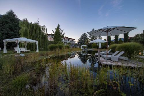a garden with tables and umbrellas and a pond at Hotel Weingarten in Appiano sulla Strada del Vino