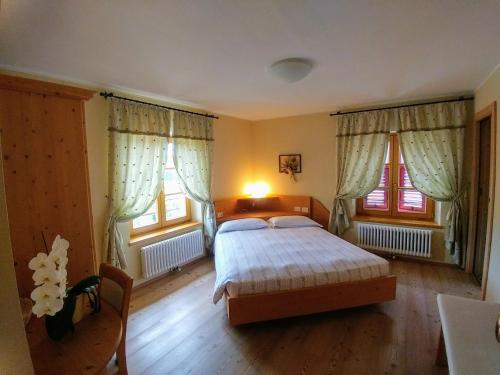 a bedroom with a bed and two windows at Agritur Maso San Bartolomeo in Romeno