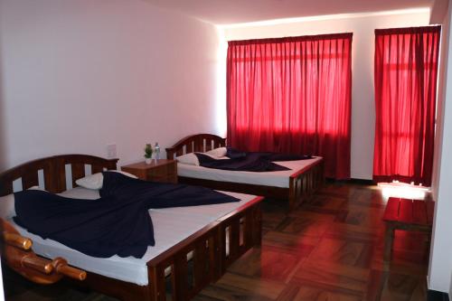 two beds in a room with red curtains at Queens rest inn in Haputale