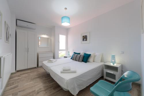 une chambre blanche avec un grand lit et une chaise bleue dans l'établissement Bungalow tipo duplex en Sonneland, Maspalomas, à Maspalomas