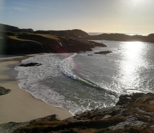 a beach with the sun shining on the water at Achmelvich View self catering in Lochinver