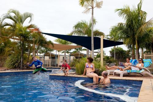 a group of people sitting around a pool at a resort at Discovery Parks - Fraser Street, Hervey Bay in Hervey Bay