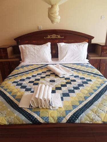 a bed with a checkered blanket with two pairs of slippers on it at Delta Suites in Kampala