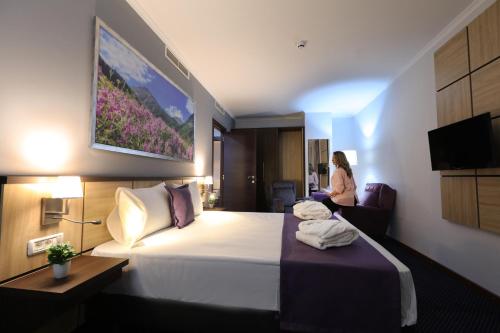 a hotel room with a bed and a woman sitting in a chair at Mercure Tetovo in Tetovo