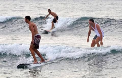 three men riding waves on surfboards in the ocean at Made Roejas Family in Uluwatu