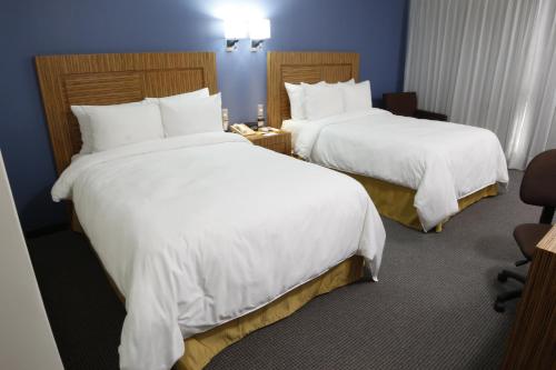 two beds in a hotel room with white sheets at Radisson Hotel & Convention Center Toluca in Toluca