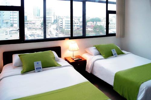 2 camas en una habitación con ventanas grandes en Hotel Castell en Guayaquil