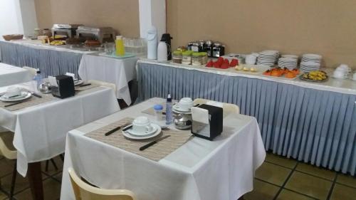a row of tables with white clothed tables with plates and dishes at Sambura Hotel in Feira de Santana