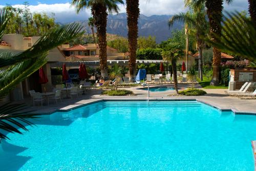 a large blue swimming pool with palm trees and mountains at The Oasis Resort in Palm Springs