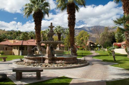 a fountain in a park with a bench and palm trees at The Oasis Resort in Palm Springs