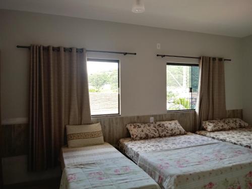 two beds in a room with two windows at Pousada Nossa Casa in Aparecida