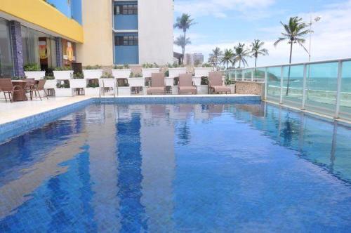 a swimming pool in a hotel with chairs and the ocean at Bahia Flat in Salvador