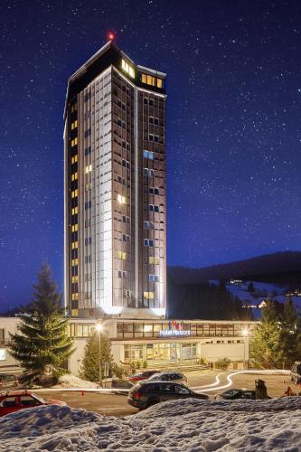 a tall building with cars parked in a parking lot at Hotel Horizont in Pec pod Sněžkou