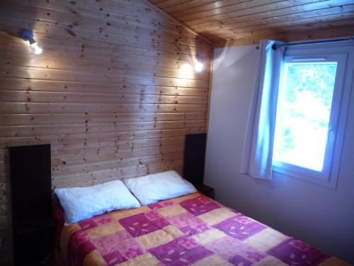 een slaapkamer met een bed met een houten muur bij Le Chalets du lac de Ganivet in Ribennes