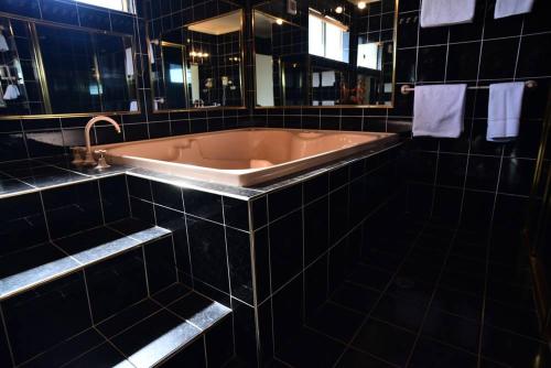 uma banheira numa casa de banho com azulejos pretos e um lavatório em The Crossing Motel em Junee