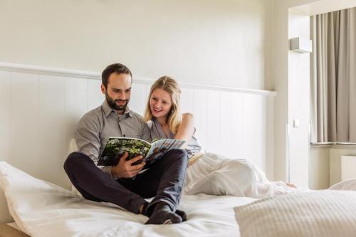 a man and woman sitting on a bed reading a magazine at West Bay in Middelkerke