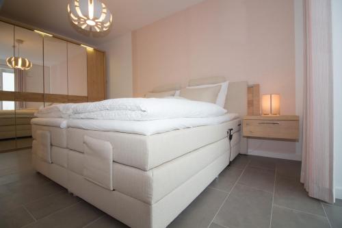 a large white bed in a bedroom with a chandelier at Wohnen am Yachthafen W48 in Cuxhaven