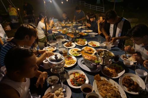 un grupo de personas sentadas alrededor de una larga mesa llena de comida en Green River Hill Resort, en Si Sawat