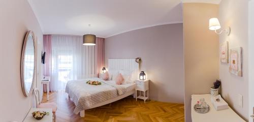 a white bedroom with a bed and a mirror at Aurora Vendégház in Hévíz