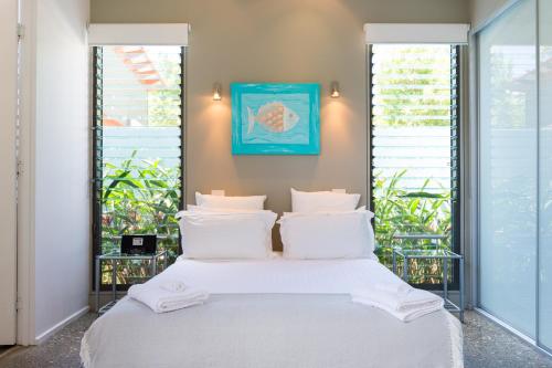 a bed with white sheets and pillows in a room with windows at By the Beach B&B Self Contained Apartments in Sanctuary Point