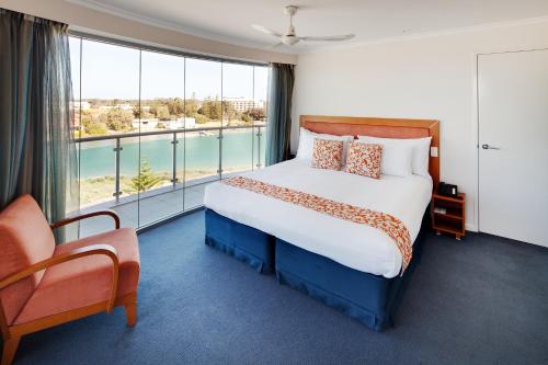 a bedroom with a bed, chair and a window at Seashells Mandurah in Mandurah
