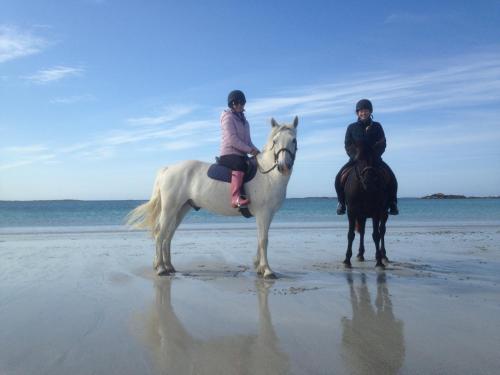 two people riding on horses on the beach at Beachcomber Cottages in Ballyconneely