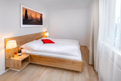 a small bedroom with a bed and a nightstand with a red pillow at CityWest Apartments in Prague