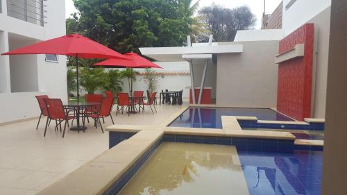 basen ze stołami, krzesłami i czerwonymi parasolami w obiekcie Casa Murillo Hotel w mieście San Juan del Cesar