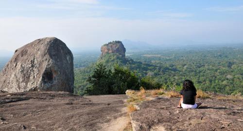 a woman sitting on a rock looking out at a view at Kings Village Sigiriya in Sigiriya
