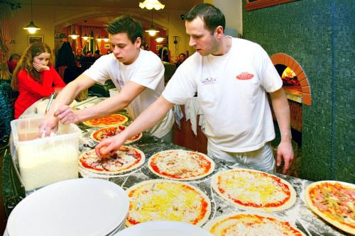 two men preparing pizzas on a table in a restaurant at Hotel pizzeria Belmonte in Špindlerův Mlýn