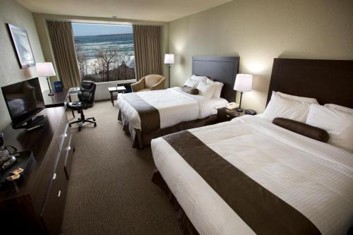 a hotel room with two beds and a television at The Oakes Hotel Overlooking the Falls in Niagara Falls