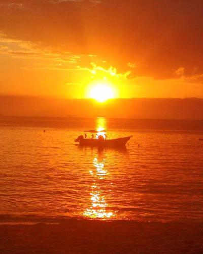 a boat in the ocean with the sun setting at Pousada Tony Montana in Praia de Araçatiba