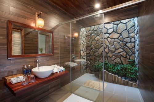 La salle de bains est pourvue d'un lavabo et d'une douche avec un mur en pierre. dans l'établissement Golden Topaz Phu Quoc Resort, à Duong Dong