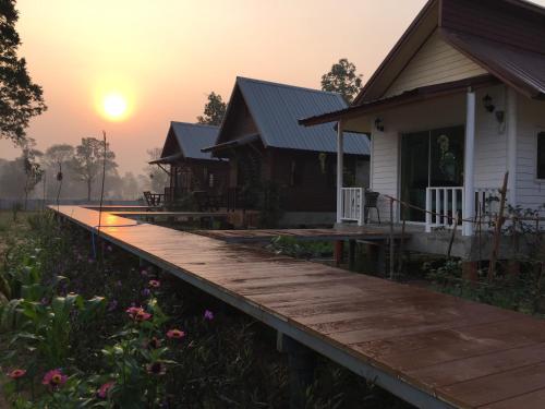 a house with a wooden deck in front of a sunset at Baan Thung Home Stay in Prasat