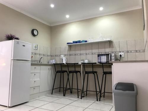 a kitchen with a white refrigerator and bar stools at Bay Breeze Guesthouse Selfcatering in Gordonʼs Bay