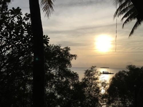 a sunset over the ocean with a boat in the water at Roos Guesthouse in Moalboal