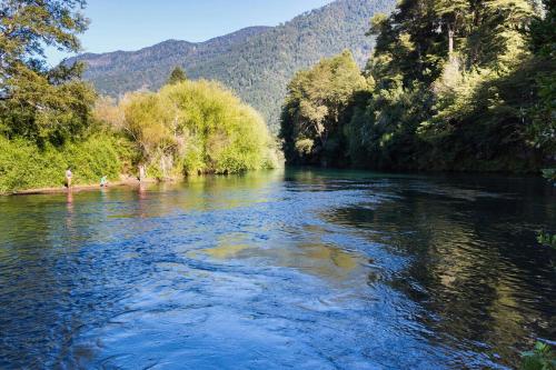 a river with trees and mountains in the background at Cabañas Los Canelos Pucon, Hermosa Granja de 20 hectaréas a orillas del Río Liucura in Pucón