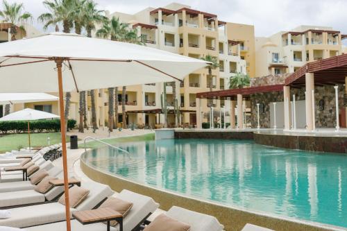 a swimming pool with chairs and an umbrella and some buildings at Pueblo Bonito Pacifica Golf & Spa Resort - All Inclusive - Adults Only in Cabo San Lucas